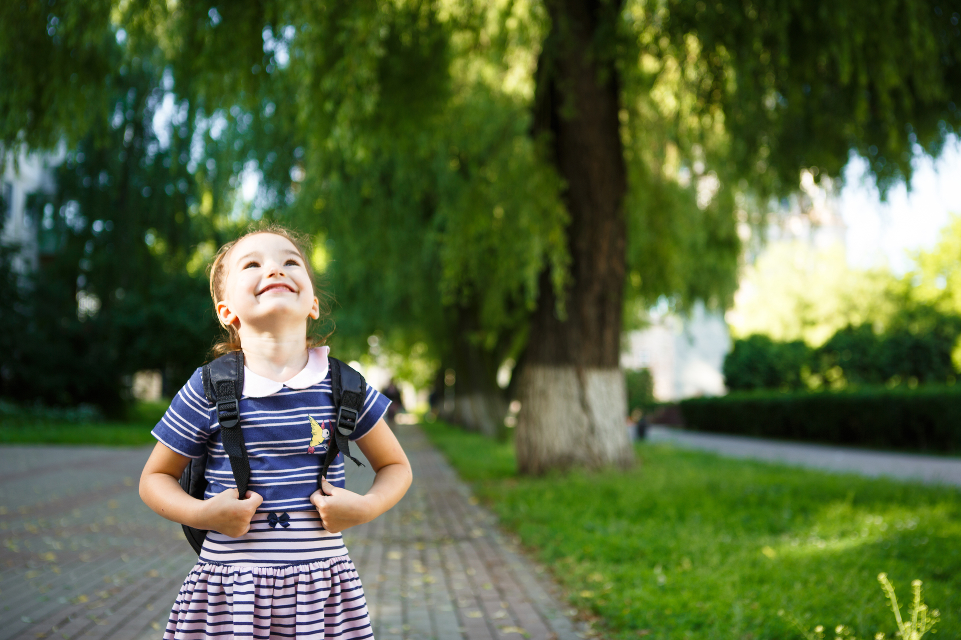 A little girl in a school uniform with a backpack and the book. Concept back to school. Elementary school, developing activities for preschoolers. Space for text